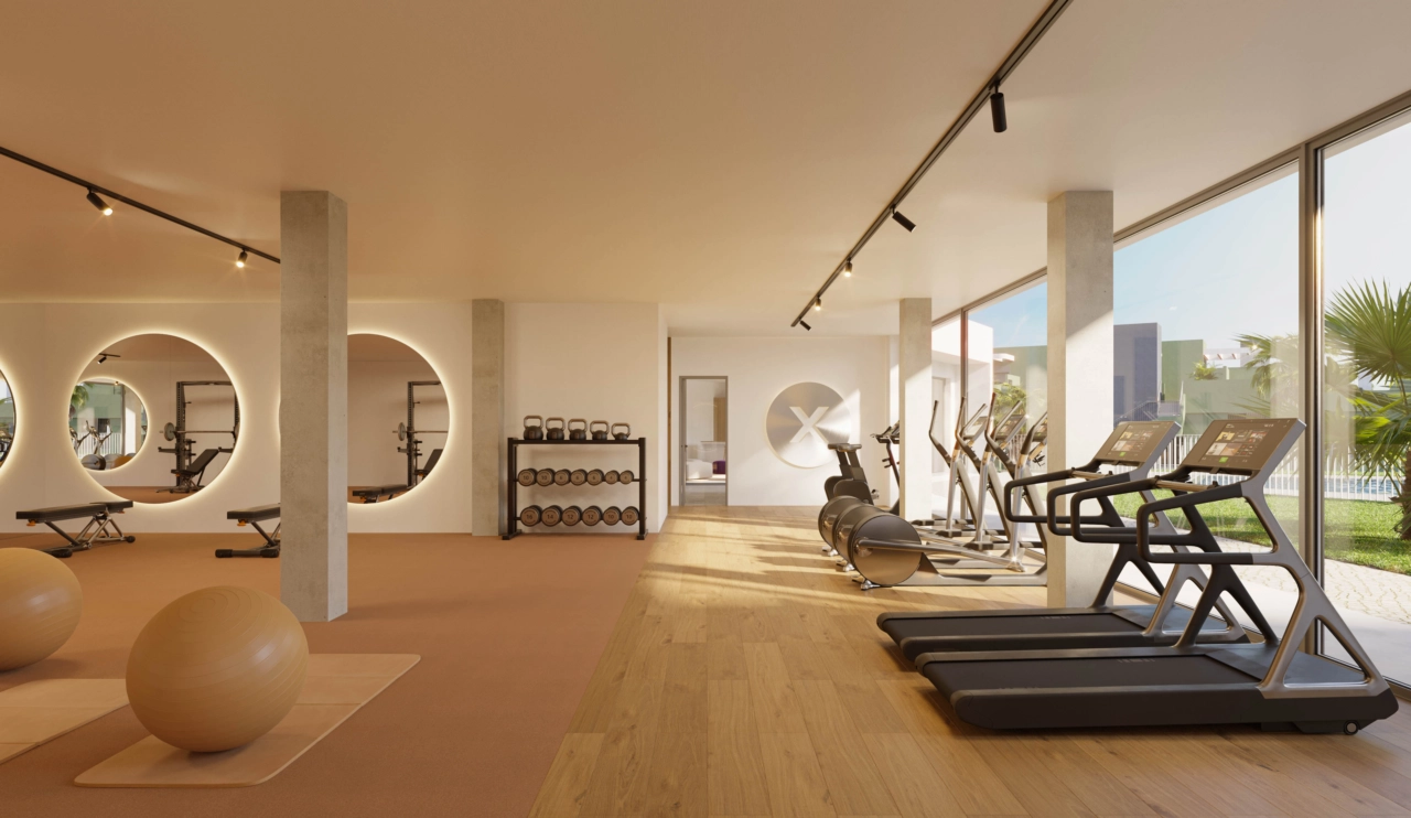 Ett fullt utrustat gym med stora fönster som vetter mot trädgårdarna och poolområdet.