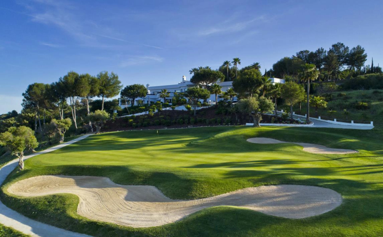 Det prestigefyllda klubbhuset på Estepona Golf, bara en kort promenad från din lägenhet, med välskötta greener i bakgrunden.